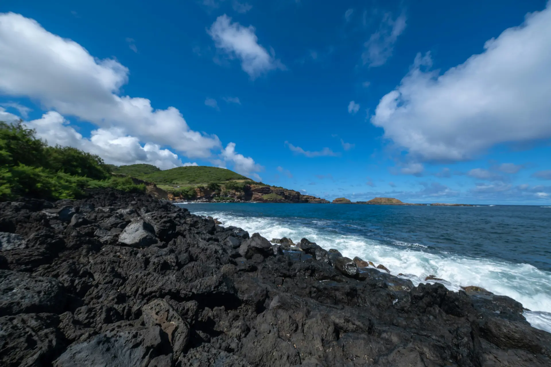 Dark volcanic rock along a coast under a blue sky with white clouds