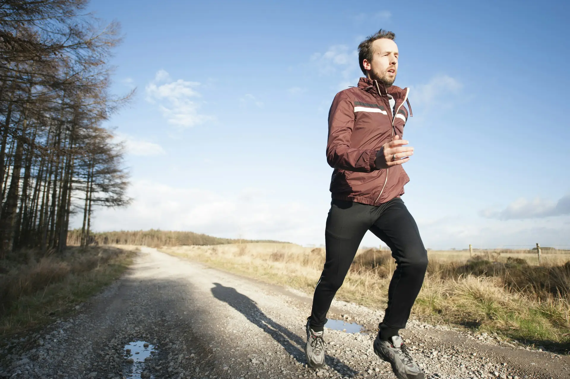 A man of about forty runs along a gravel road under a blue sky