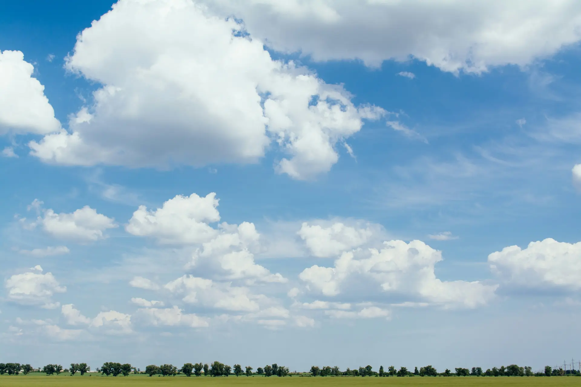 A big sky of white clouds over a strip of plain and trees